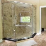 A modern corner shower with glass walls and beige tile interior, featuring a reflective chrome handle and fixtures, perfect for a bathroom remodel and with a view of a window inside the shower.