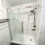 A modern bathroom design featuring a glass-enclosed shower stall with a white marble-like interior, a black shower system, and an elegant bathtub.