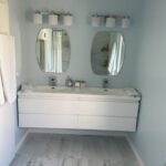 A modern bathroom remodel featuring a double vanity with white cabinetry, two rectangular mirrors, and a light blue wall.