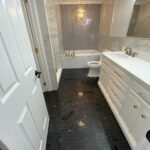 Modern bathroom design featuring hexagonal black floor tiles, white cabinetry, marble walls, and gold fixtures.
