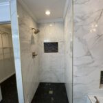 A modern bathroom design with a walk-in shower featuring white marble walls and dark hexagonal floor tiles.